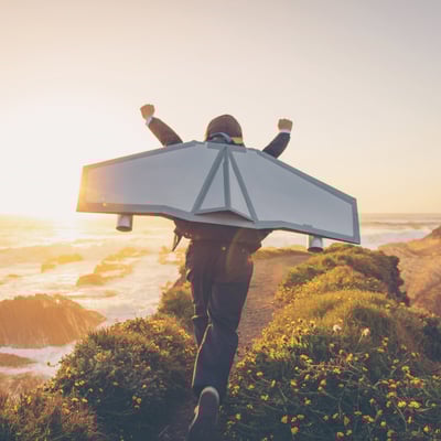 child-running-along-clifftop-with-toy-wings