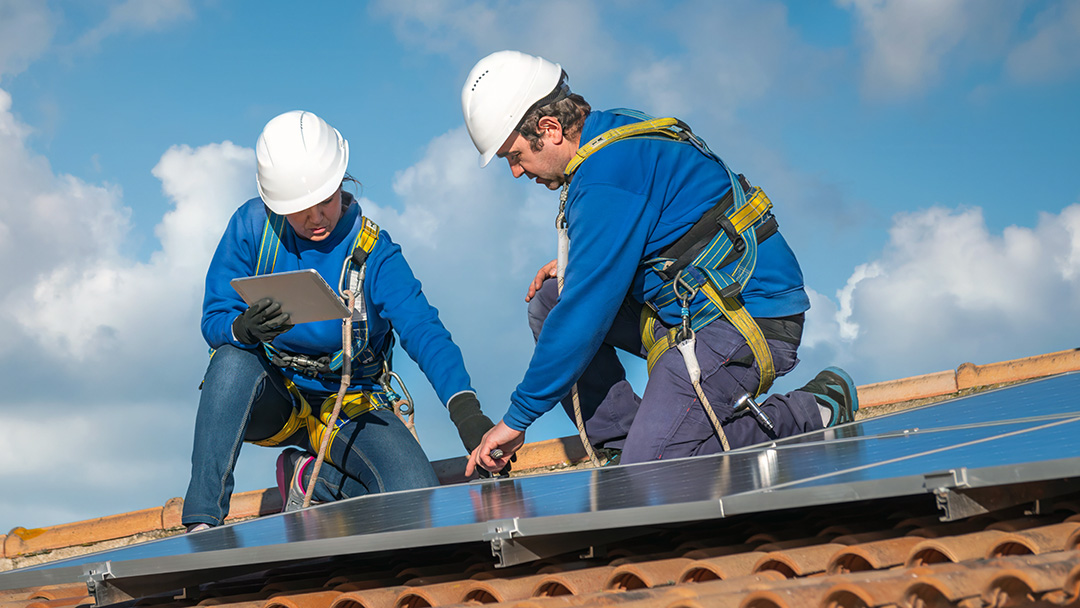 Workers installing solar panels on a practice roof
