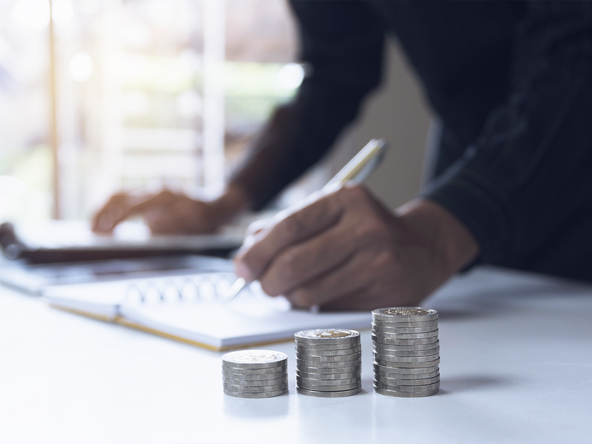 Businessman making financial notes in a notebook, with coins in the foreground