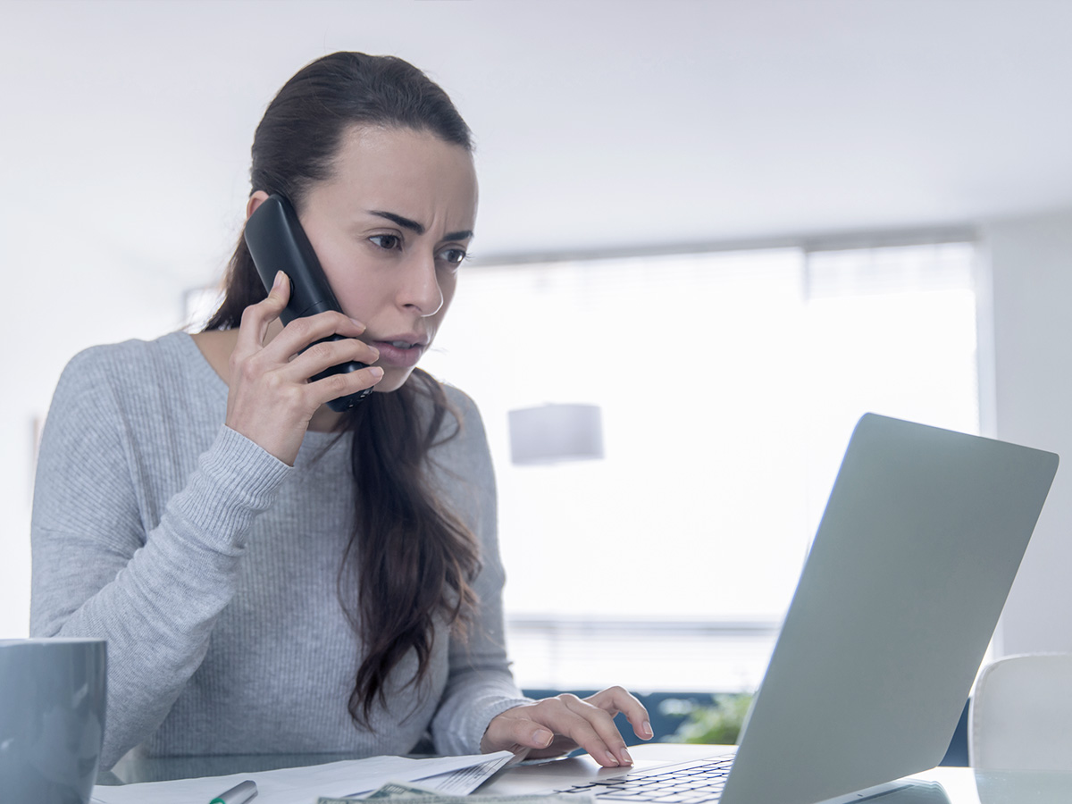 Woman on phone in front of laptop, making complaint