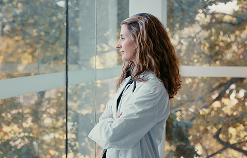 Doctor looking out-of hospital window at foliage