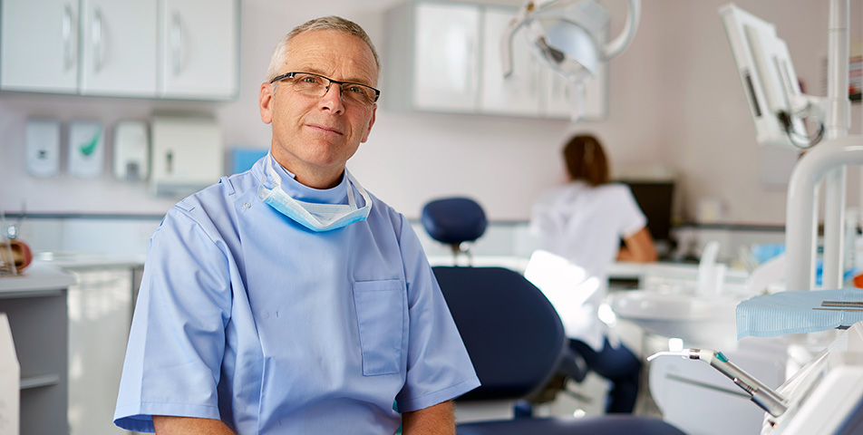 Dentist in glasses facing camera in practice